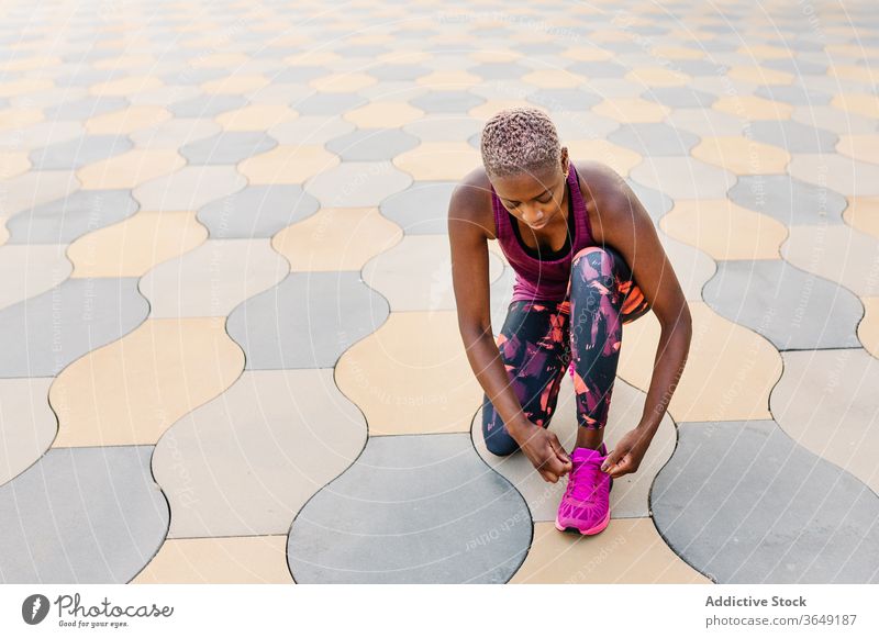 Afroamerikanischer Athlet bindet während des Trainings Schnürsenkel an Turnschuhen Sportlerin Krawatte Schuhbänder Großstadt Kniebeuge Pause Straßenbelag
