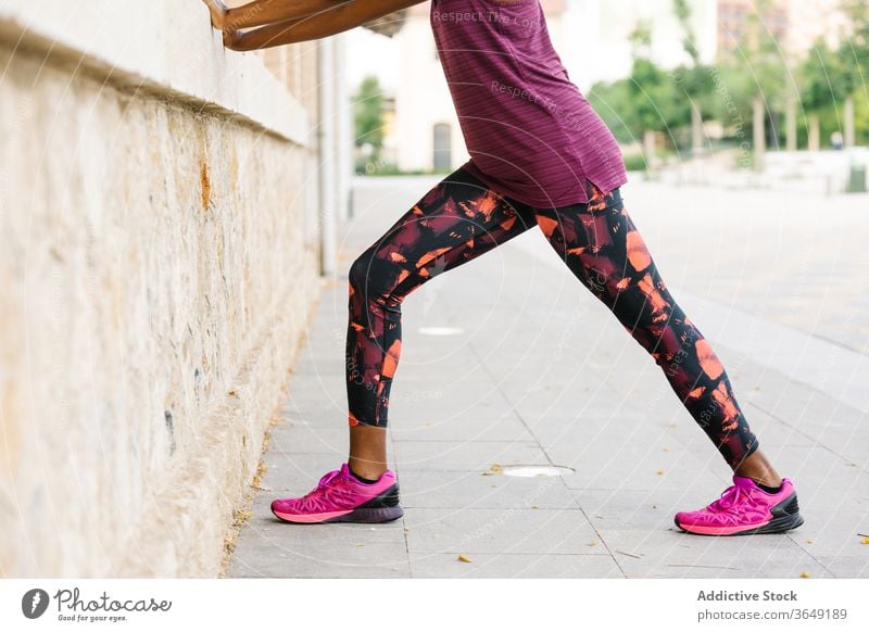 Schwarze Sportlerin, die sich auf dem Bürgersteig in der Nähe eines Backsteinhauses die Beine vertritt Dehnung Übung üben Aktivität Sportbekleidung Gebäude