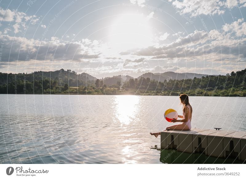 Frau sitzt am Rand einer Mole in der Nähe des Sees Beachball spielen Teich Sommer Badebekleidung Feiertag sitzen Urlaub genießen aufblasbar Gummi Wasser