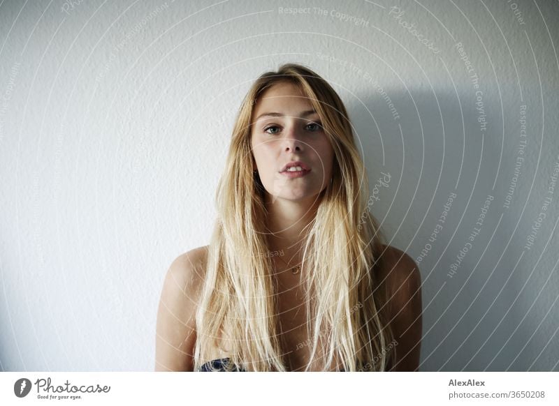 Portrait einer schönen, jungen, blonden Frau vor einer weißen Wand junge Frau schlank langhaarig ästhetisch Model Identität sportlich Zentralperspektive
