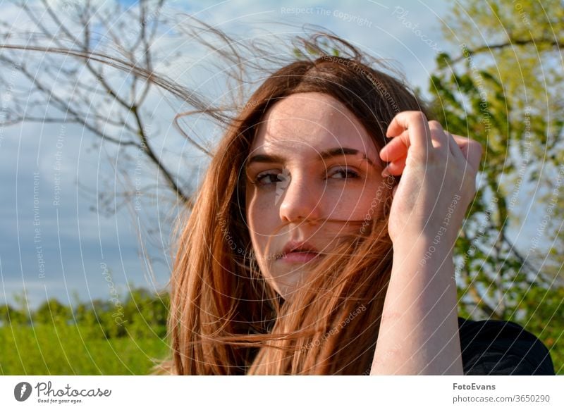 Mädchen steht mit wehendem Haar in der Natur, Hand auf dem Kopf Arme Wind Porträt Mode Tag Schönheit modern attraktiv Baum im Freien Sonnenlicht echte Person