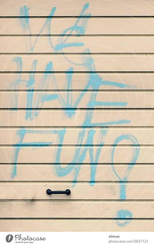 "WE HAVE FUN" steht in großer hellblauer Graffiti - Druckschrift auf einem beigefarbenen Metall-Garagentor über dem Griff we have fun Schmiererei