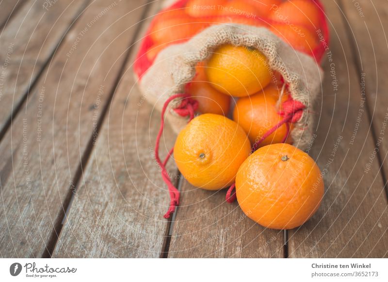 Ein geöffneter Beutel mit Mandarinen liegt auf einem älteren Holztisch. Zwei Früchte liegen vor dem Beutel. Nahaufnahme mit schwacher Tiefenschärfe