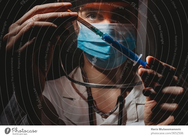 Ärztin mit Maske und Schild, die den Impfstoff in den Händen hält, auf schwarzem Hintergrund 2020 Atemschutzmaske schwarzer Hintergrund Klinik Korona-Epidemie
