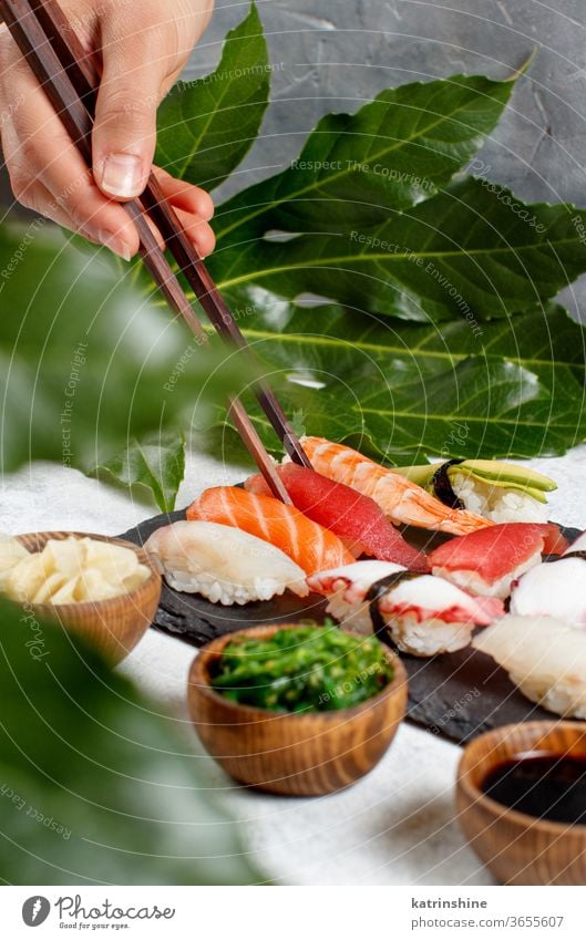 Nahaufnahme einer Hand, die ein Suchi mit Stäbchen von einem Teller nimmt Sushi unter Essstäbchen verzehrfertig Essen Sashimi Brötchen Sushi-Bar Blatt
