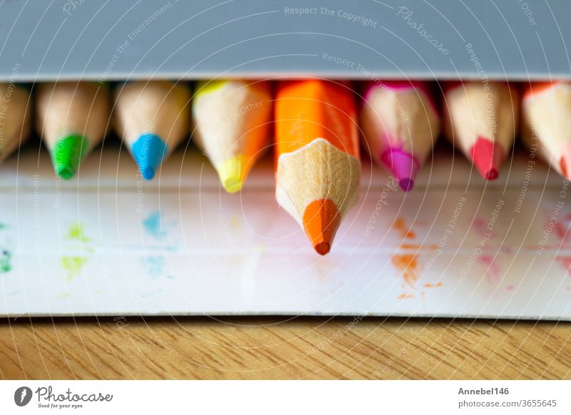 Farbstifte in einer kartongrauen Schachtel, Regenbogenfarben, orangefarbener Bleistift ragt aus Makro-, Schul- oder Büromaterial Farbe gelb rot Kunst Zeichnung