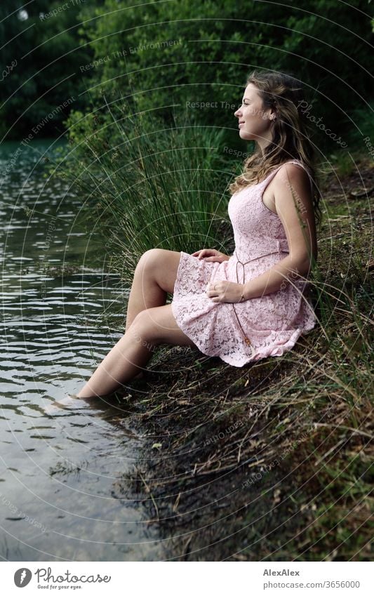 Junge Frau in rosa Sommerkleid sitzt auf einer Waldlichtung mit den Füssen im Waldsee Mädchen Gras Pflanzen Laub grün Natur Kleid barfuß barfüßig schlank