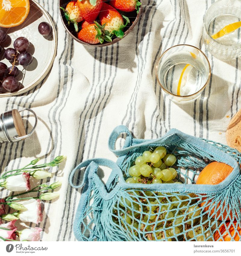 Sommerpicknick Flatlay, Früchte, Beeren und Zitronenwasser auf gestreifter Baumwolldecke Picknick Lebensmittel Essen Diät frisch Brille Wasser Zitrusfrüchte