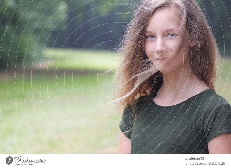 Porträt eines lächelnden Mädchens mit Wind in den Haaren im Park Halbprofil Bewegungsunschärfe Schatten Licht Tag Außenaufnahme Farbfoto Pubertät Gefühle