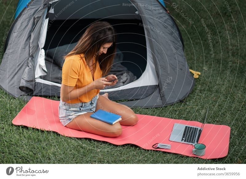 Junge Frau benutzt Geräte beim Camping Lager Apparatur benutzend Smartphone modern Zelt Tourist positiv Natur jung lässig Laptop Wiese Browsen ruhen Urlaub
