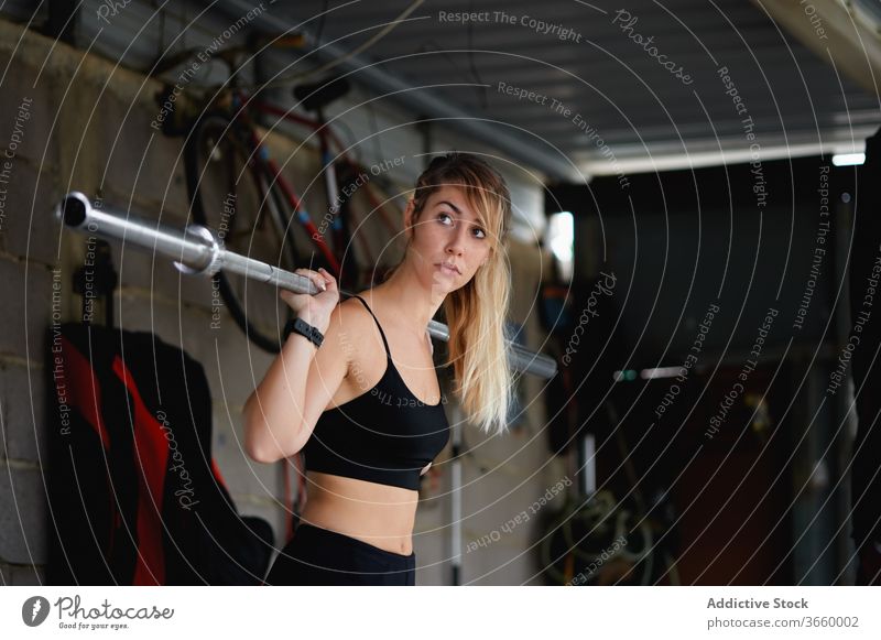 Schlanke Sportlerin beim Training mit Langhantel im Fitnessstudio Curl-Hantel Übung Konzentration passen Gerät sportlich Fokus Körper Sportkleidung stark