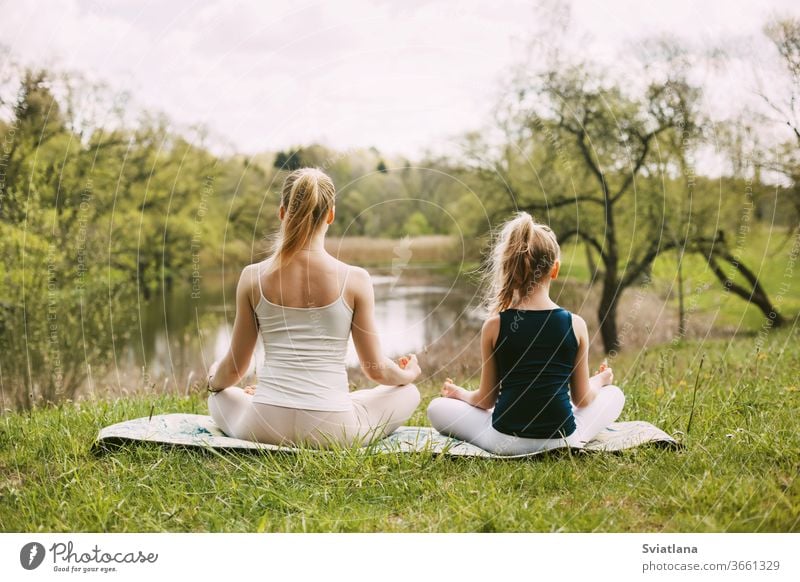Mutter und Tochter sitzen in der Lotus-Position im Garten. Die Familie praktiziert Yoga im Freien. Rückansicht, Platz für Text Meditation Lotos Zusammensein