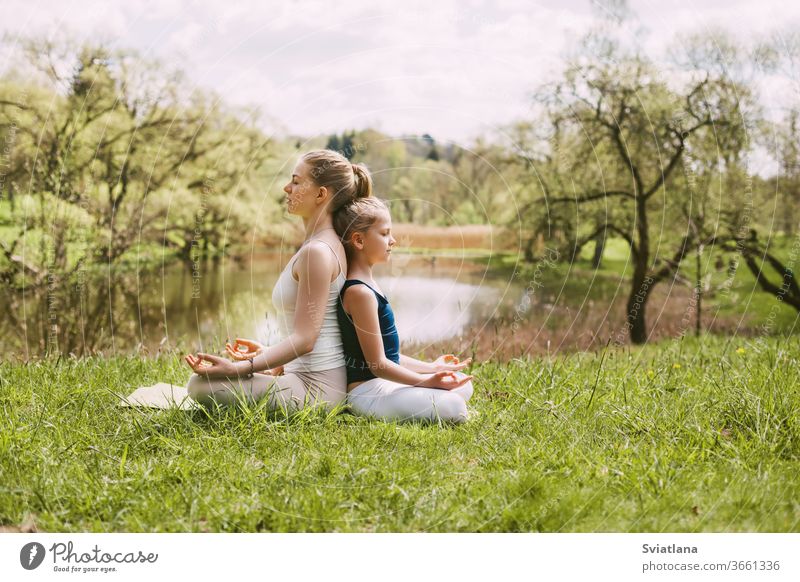 Eine schöne junge Frau und ein blondes Mädchen meditieren in der Lotus-Position. Familienurlaub, Meditation. Seitenansicht, Platz für Text Yoga im Freien Lotos