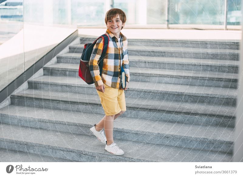 Ein glücklicher Junge mit einem Rucksack und einem Buch geht zur Schule. Beginn des neuen Schuljahres nach den Sommerferien. Zurück zur Schule Kind Rücken