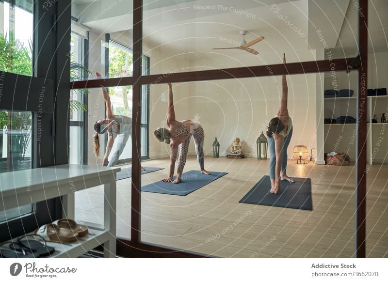 Flexible junge Yogalehrerinnen, die im Lichtstudio eine Pose mit erweitertem Seitenwinkel einnehmen Frauen üben Dehnung Gesundheit Wellness Klasse