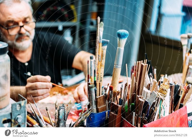 Männlicher Künstler arbeitet hinter einer Reihe verschiedener Pinsel Pinselblume Kunst Designer Arbeitsplatz Atelier Sammlung Kleinunternehmen Skizze Fokus