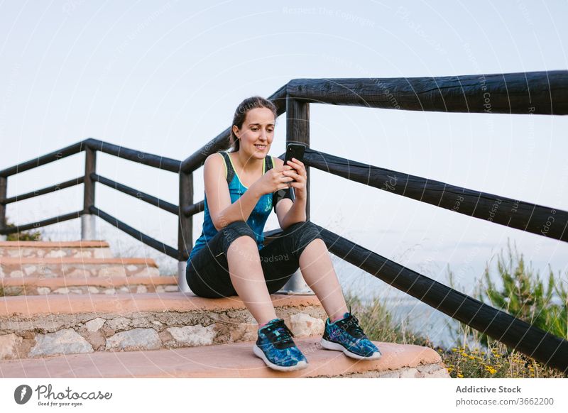 Sportlerin auf Treppe sitzend mit Mobiltelefon in Meeresnähe Pause MEER ruhen allein Sportbekleidung Athlet Treppenhaus Gesundheit passen Wohlbefinden Sommer