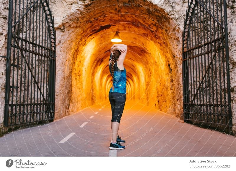 Sportlerin, die während des Trainings im Tunnel die Arme streckt Dehnung Aufwärmen Übung Armbinde Stollen Wand rau Sportbekleidung Athlet Gesundheit passen