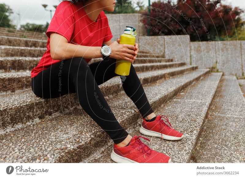 Durstige ethnische Sportlerin trinkt nach dem Training Wasser auf der Treppe trinken Thermoskanne Sportbekleidung Pause Hydrat Augen geschlossen