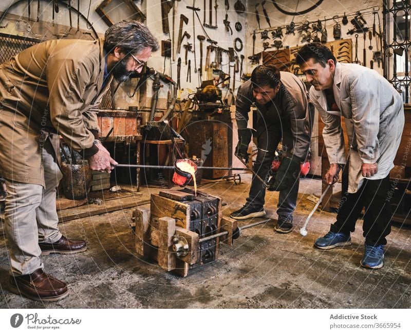 Gruppe von Handwerkern, die eine Form mit Metall füllen Metallarbeiten gießen Schimmelpilze heiß zerlaufen eingießen besetzen Goldschmied Prozess Arbeit Männer