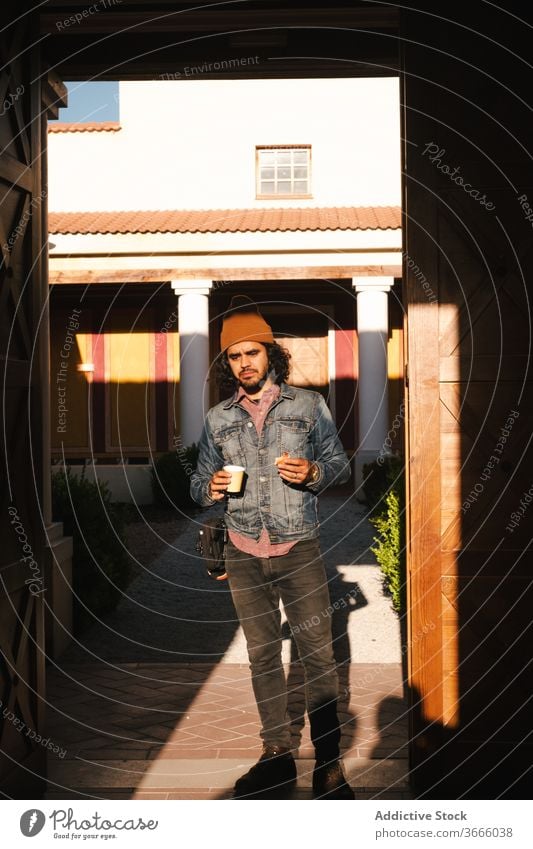Mann mit Pappbecher gegen Gebäude mit Säulen Erfrischung trinken positiv Straße Außenseite Hipster Kaffeepause Inhalt Outfit farbenfroh Abend Sonnenlicht Pause