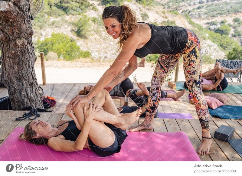 Glückliche Frau, die während des Yoga-Kurses mit Trainerin die Beine streckt Frauen liegende Taube supta kapotasana Dehnung Wellness Gesundheit positiv Asana