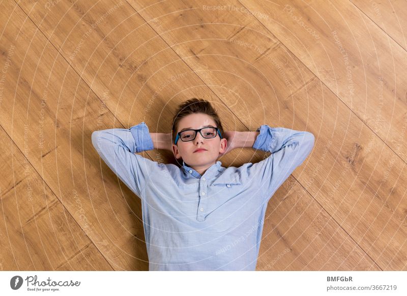 Teenager mit Brille liegt entspannt auf Holzboden zu Hause Junge liegen Boden Holzbolden Parkett Homeschooling Oberkörper Teenie jugendlicher zu Hause bleiben