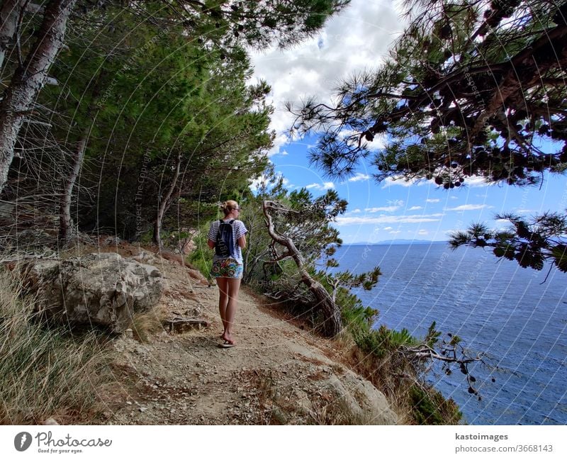 Junge Frau in den Sommerferien, die auf einem Küstenpfad durch Kiefernwald wandert, der kleine Buchten des adriatischen Mittelmeers verbindet. Mädchen Weg