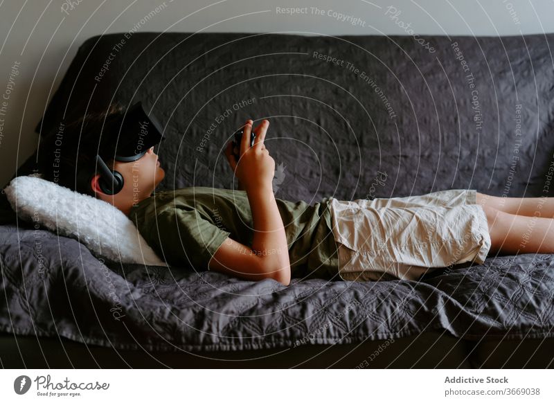 Kleiner Junge mit VR-Headset entspannt zu Hause auf der Couch Kind Sofa Schutzbrille Gamepad spielen Gerät unterhalten digital Innovation Apparatur modern wenig