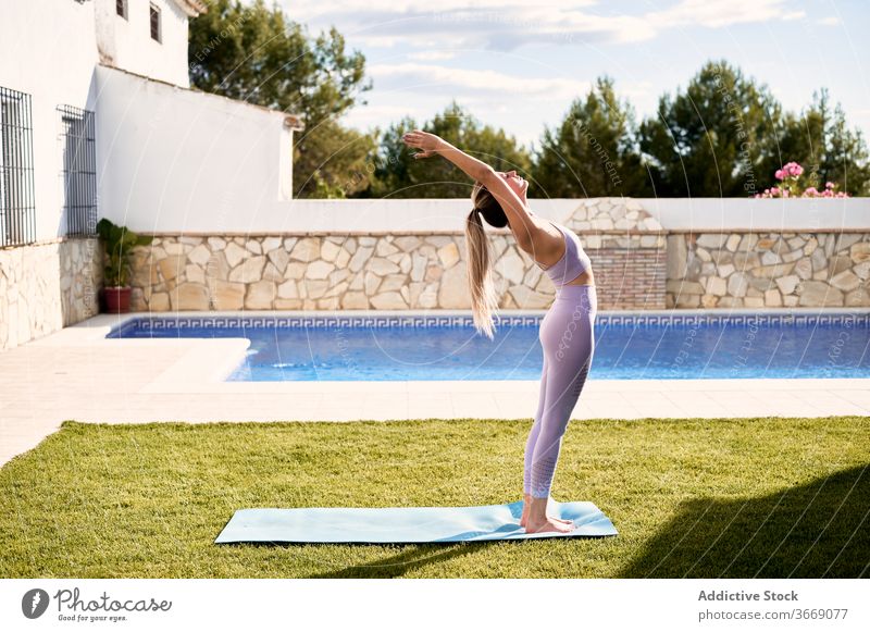 Ruhige Frau macht Yoga in Bergposition auf der Terrasse Berg-Pose urdhva hastasana üben Asana Sommer Unterlage Stressabbau schlank BH Leggings Pool Windstille