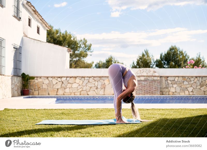 Frau macht Yoga in Uttanasana auf der Terrasse Vorwärtsbeuge üben uttanasana beweglich Asana Pose Rasen Sportbekleidung Wegbiegung Unterlage Gesundheit Übung