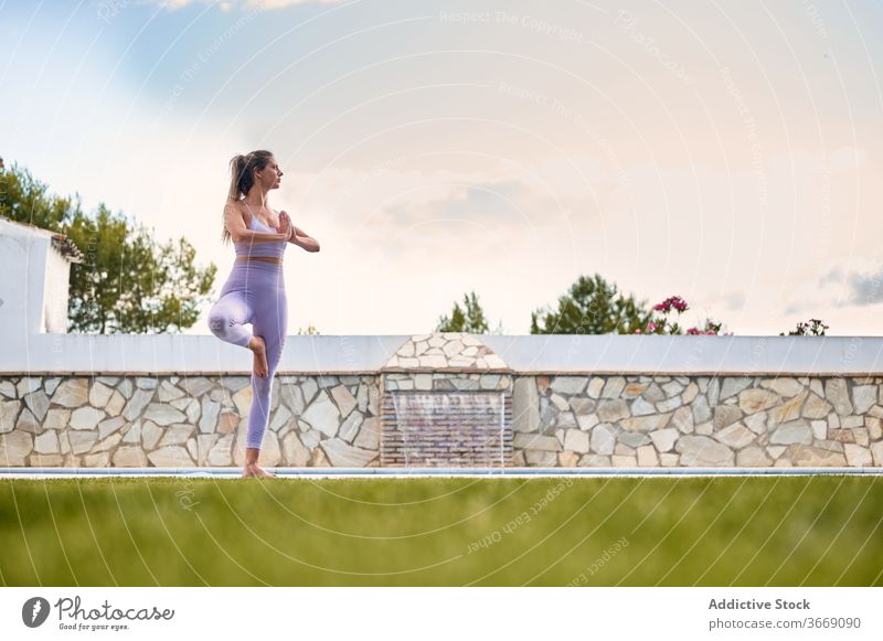 Ruhige Frau übt Yoga in Baum-Pose Baumhaltung Gleichgewicht vrksasana Namaste Windstille ruhig Unterlage Beckenrand Hinterhof Wasser Hof gestikulieren BH