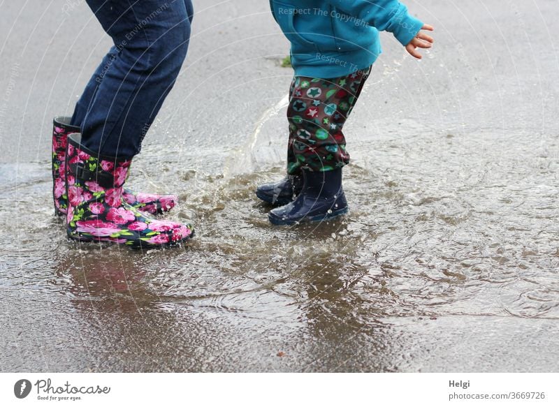 Pfützenspaß - Mutter und Kind haben Spaß beim Sprung in die Pfütze Detailaufnahme Beine Gummistiefel springen platsch Freude platschen spritzen Wasser nass