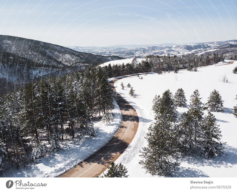 Winterlandschaft im Sonnenlicht. Blick auf die von immergrünen Bäumen umgebene Bergstraße im Winter, Drohnenschuss oben Antenne Asphalt Hintergrund Kabine kalt