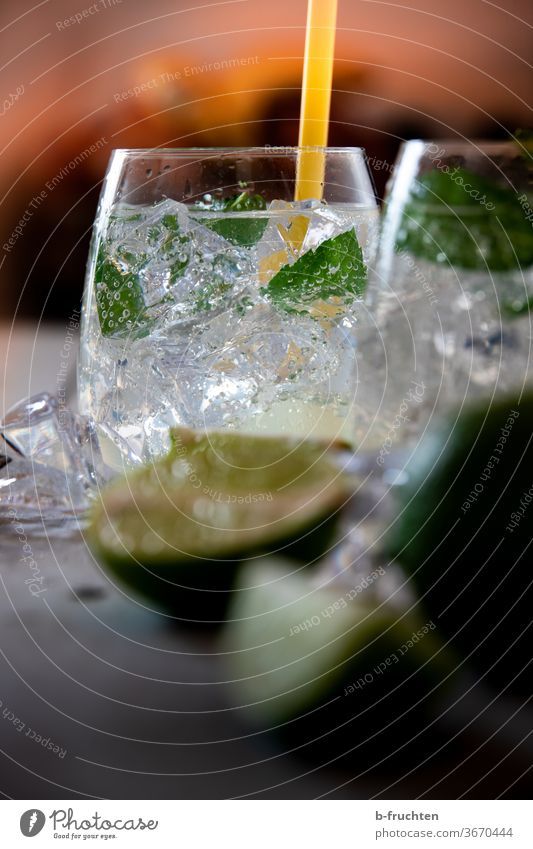 Trinkglas mit Eiswürfeln, Minze und Sodawasser. Limetten im Vordergrund Cocktail Getränk Lemon Soda Wasser Glas frisch trinken kalt Erfrischung Sommer Zitrone
