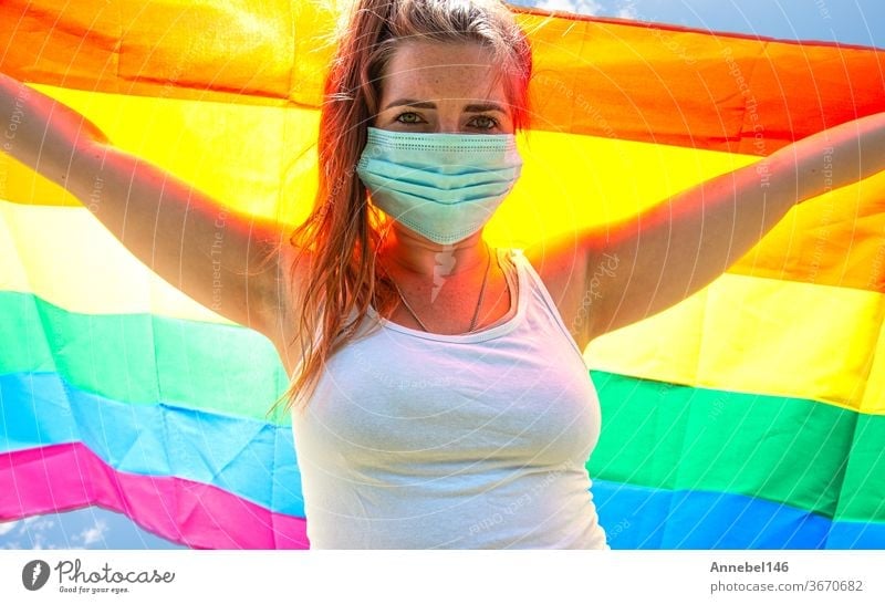 Junge Frau schwenkt Regenbogenfahne für LGBT-Rechte, Freiheit für homosexuelles Lgbtq-Konzept, trägt eine Sicherheitsmaske für Covid-19, Coronavirus. Protestierend