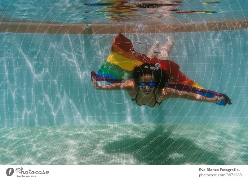 junge Frau in einem Pool, die unter Wasser eine Regenbogenflagge mit schwuler Flagge hält.LGBTQ-Konzept. Sommerzeit Schwimmbad Schwulenflagge lgbtq Beteiligung