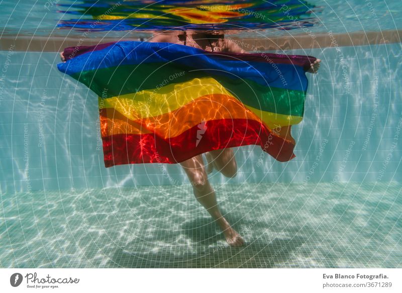 junge Frau in einem Pool, die unter Wasser eine Regenbogenflagge mit schwuler Flagge hält.LGBTQ-Konzept. Sommerzeit Schwimmbad Schwulenflagge lgbtq Beteiligung