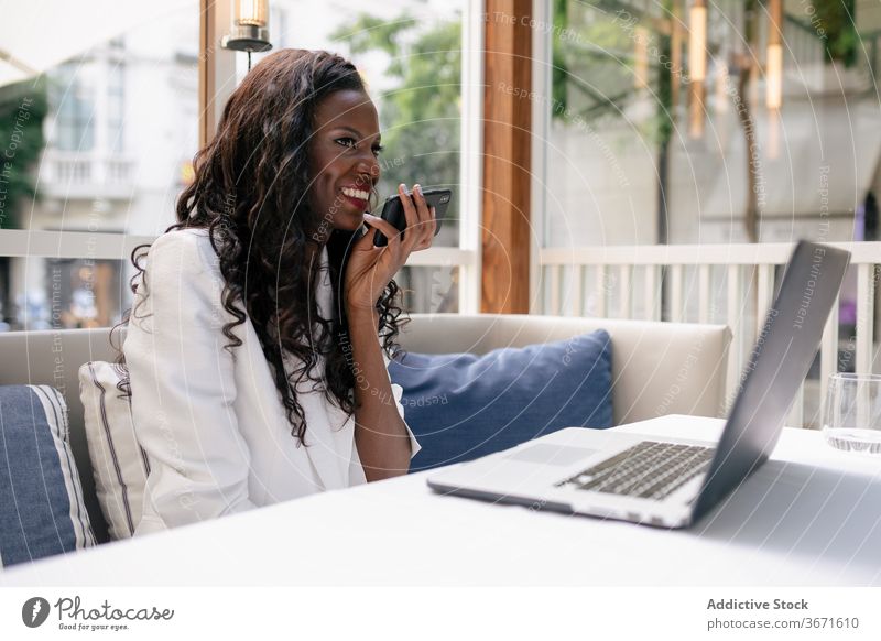 Fröhliche schwarze Geschäftsfrau mit Smartphone und Laptop Frau Inbetriebnahme Telefonanruf selbstbewusst Lachen Audiobotschaft benutzend elegant Funktelefon