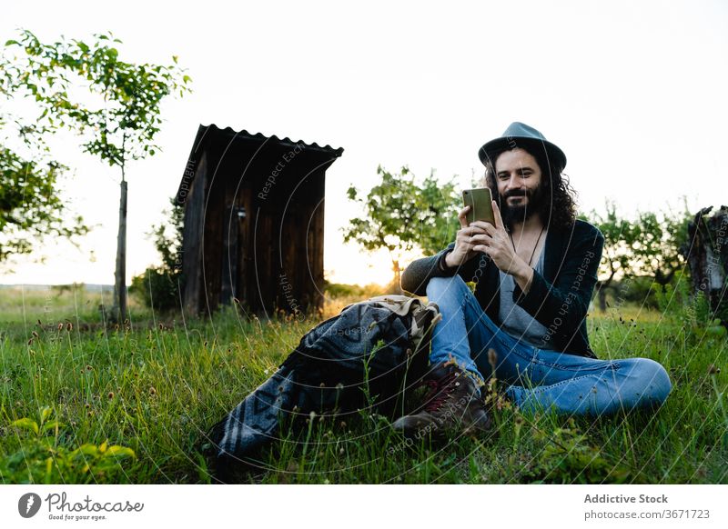 Entspannter Mann, der auf einer Wiese auf seinem Smartphone surft Hipster soziale Netzwerke Talkrunde Feld Sommer sich[Akk] entspannen benutzend männlich Natur