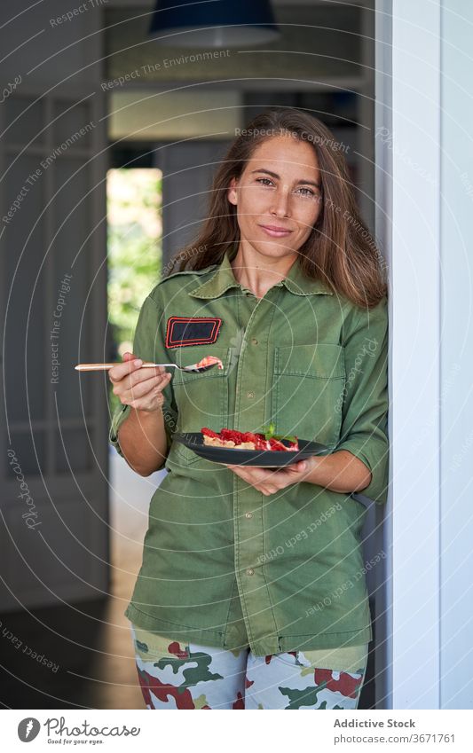 Lächelnde Frau mit Stück Kuchen zu Hause Spielfigur Pasteten selbstgemacht heimwärts Erdbeeren schmackhaft heiter Dessert geschmackvoll süß Teller Lebensmittel