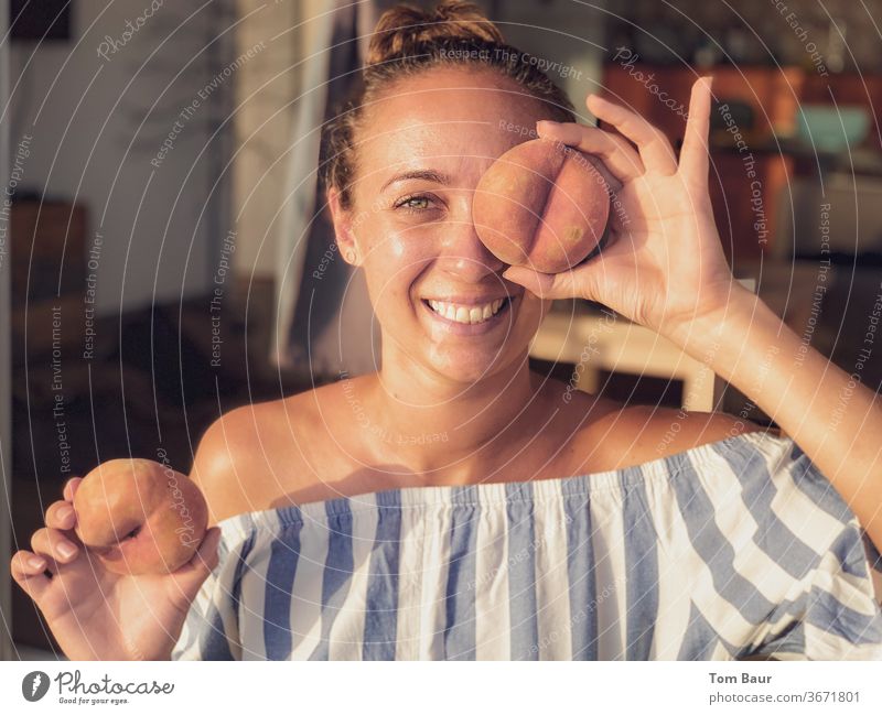 Junge Frau mit brunette Haare hält sich einen Pfirsich vors Auge Brunette lachen happy glücklich spaßig spass blau weiss Porträt Schulter Freizeit & Hobby