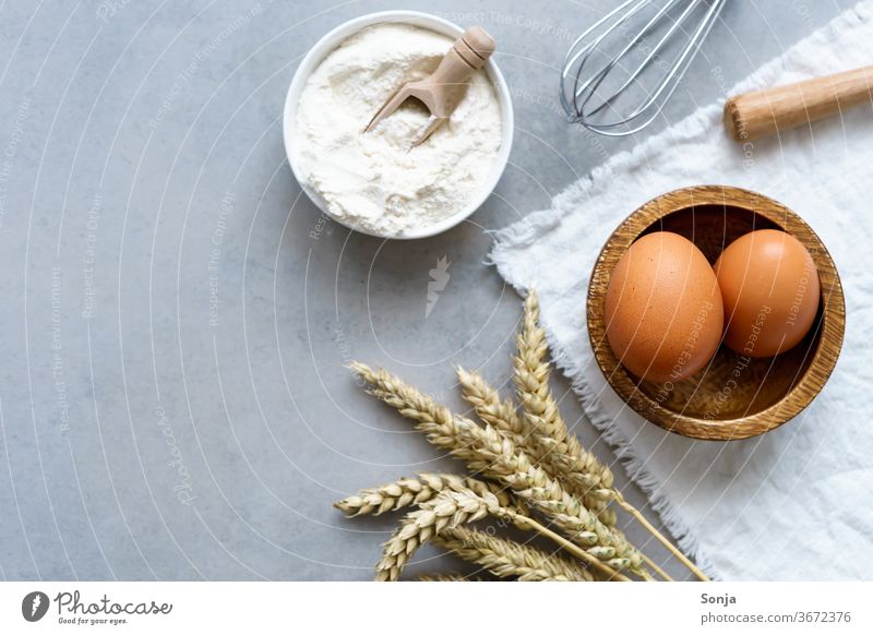 Zutaten für Kuchen und Kekse auf einem grauen Küchentisch. Weizenähre, braune Eier und Mehl, Draufsicht eier Vorbereitung Teigwaren Brot backen roh Backwaren