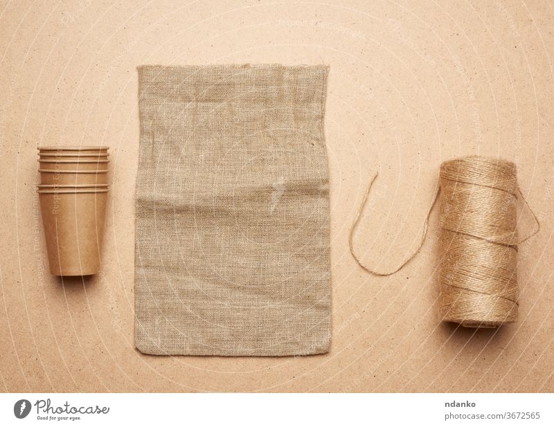 Pappbecher, Strang mit braunem Seil und leerer Tasche auf braunem Holzgrund Konzept Accessoire Hintergrund beige blanko Sackleinen Leinwand Nahaufnahme Stoff