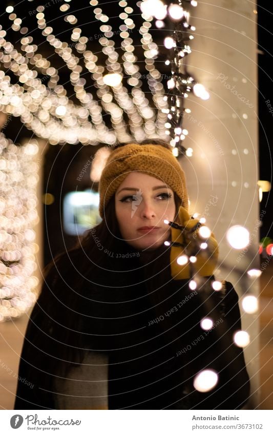 Nachtporträt einer jungen Frau, die in die Ferne schaut und sich an eine Lichterkette lehnt. Kalte Winternacht Lächeln Bokeh Mädchen schön Abend Porträt
