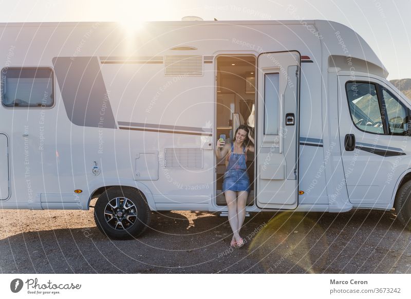Lächelnde junge Frau, die an einem sonnigen Tag ein Selfie auf ihrem am Strand geparkten Wohnmobil mitnimmt Lebensstile Kleintransporter wüst Erkundung Reise