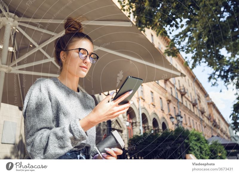 Junge stilvolle hübsche Frau mit Smartphone an der Outdoor-Café. jung Großstadt Internet Öffentlich Brille im Freien Porträt lässig Stil Lifestyle Mädchen
