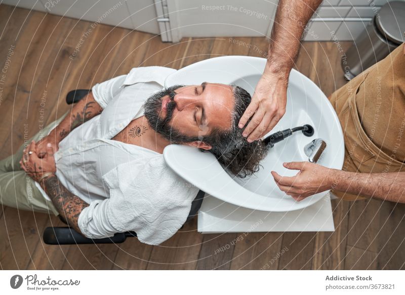 Friseur wäscht Haare eines männlichen Kunden im Salon Männer Kopf Waschbecken Barbershop Arbeitsplatz Klient Haarschnitt Dienst Vollbart Pflege professionell