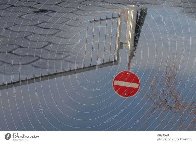 Spiegelung des Verkehrsschildes Verbot der Einfahrt in einer Wasserpfütze Schild Verbotsschild Durchfahrt verboten Pflastersteine Gehweg Zaun Tor Himmel