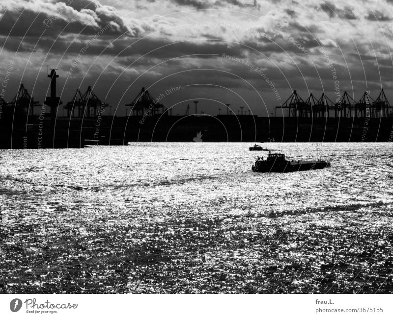 Die Elbe glitzert silbern in der Sonne, die Kräne verharren im Dunklen und staunen, während die Schiffe lautlos dahingleiten. Hamburg Hafen Wasserfahrzeug Kran